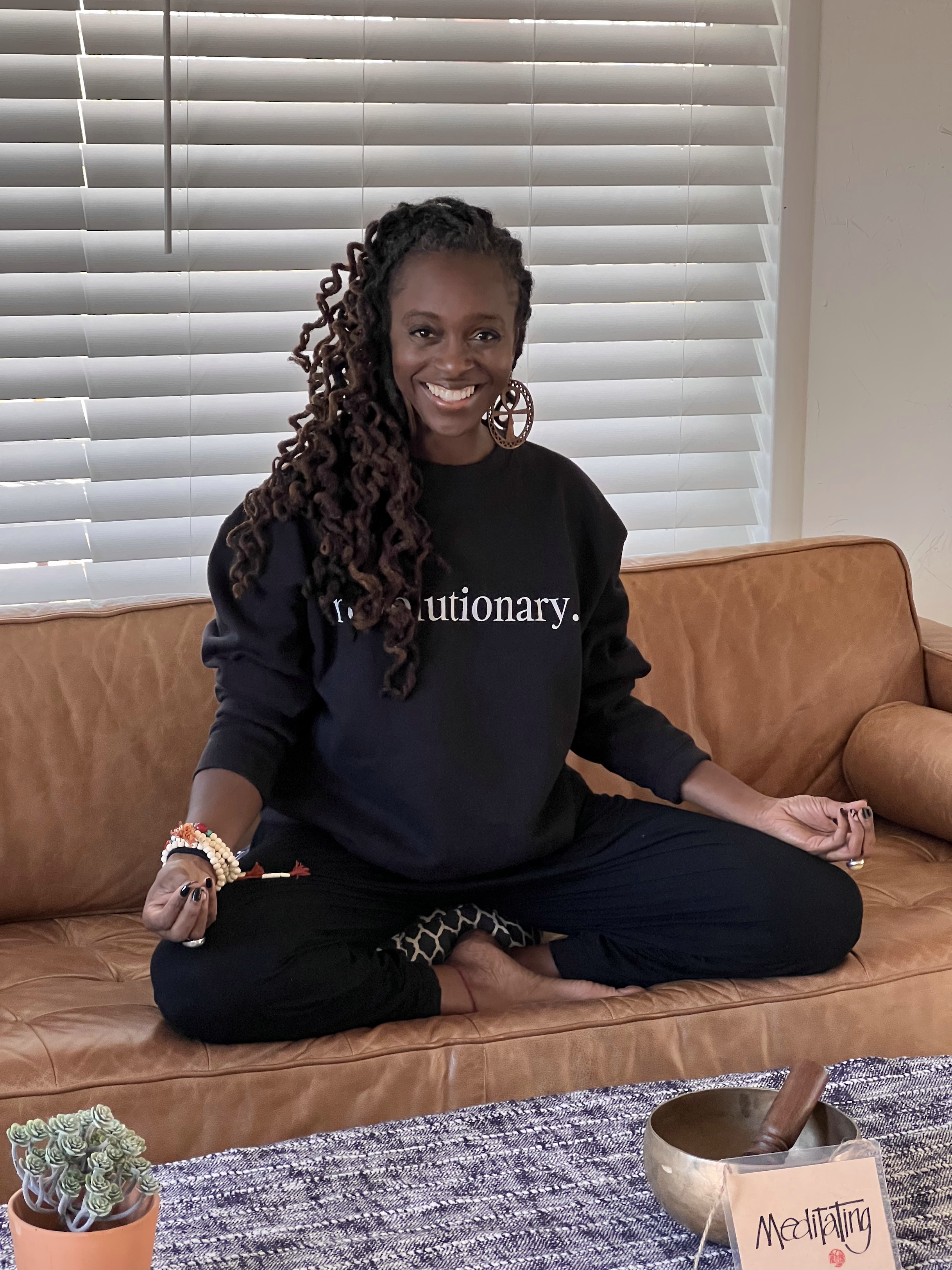 Jylani Ma'at Brown seated cross-legged, smiling, wearing a sweatshirt that reads revolutionary